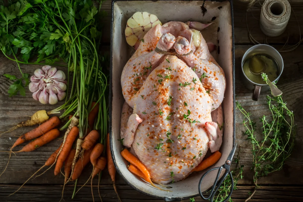 Raw chicken submerged in a clear brine solution with visible salt, herbs, and peppercorns in a glass container on a kitchen countertop, highlighting the process of brining for enhanced moisture and flavor.